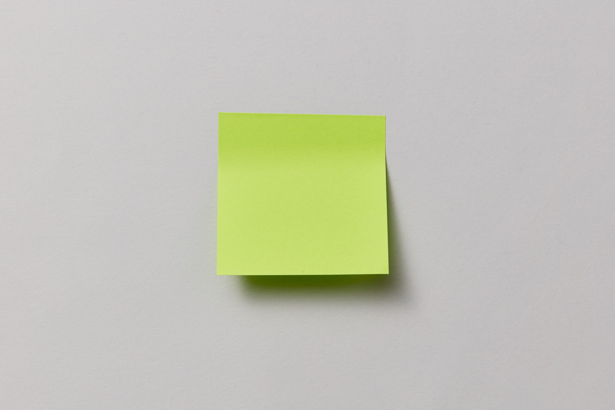 A single bright green sticky note on a neutral grey background with ample copy space.